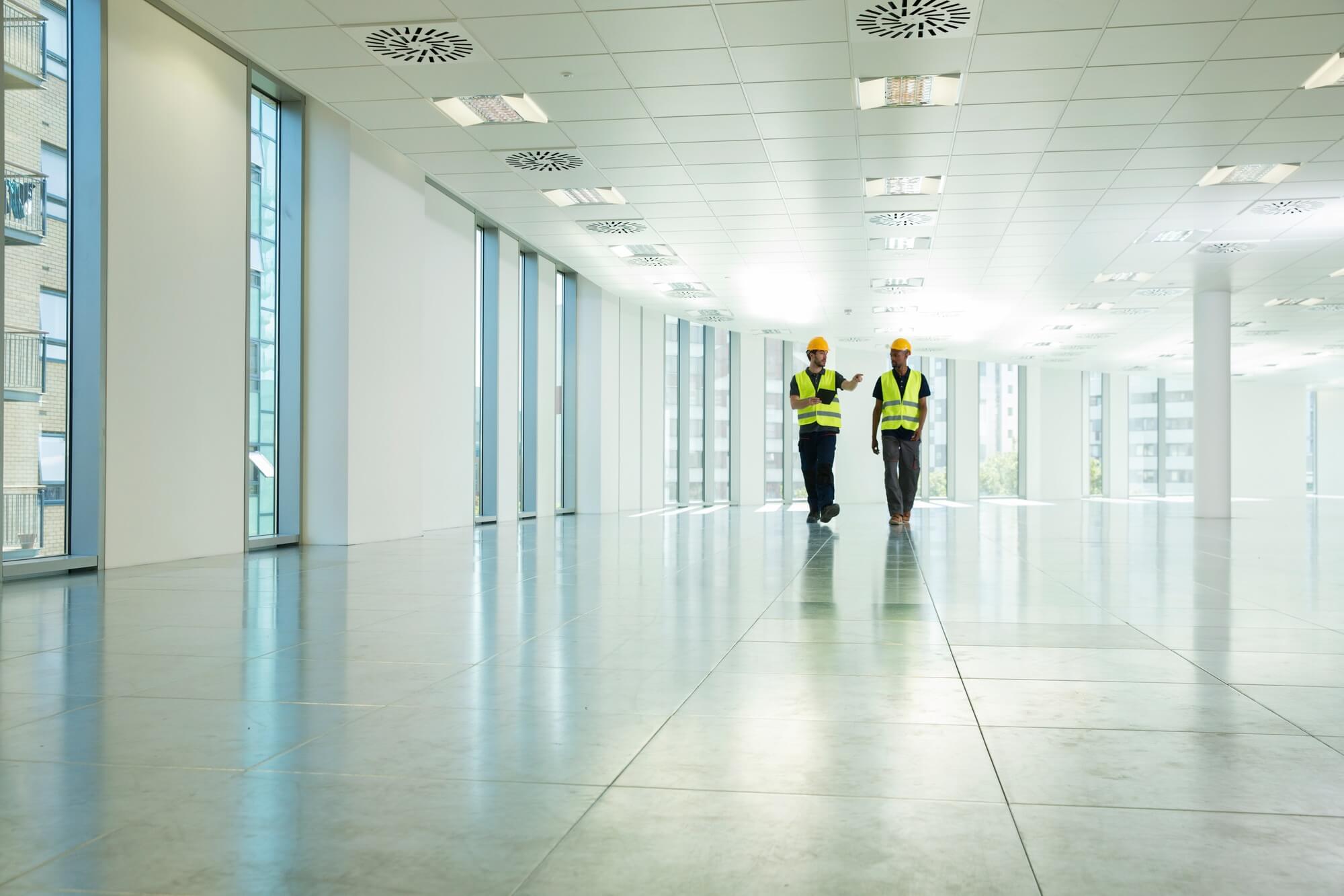 Two construction workers walking through empty office space